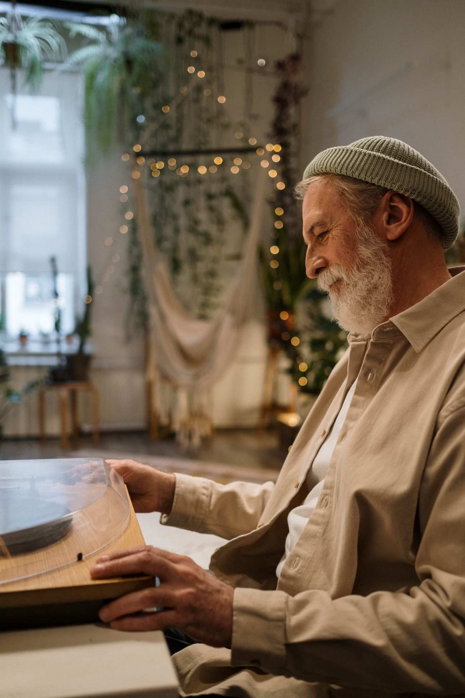 An older man with a white beard and a knit cap lifts the lid of his record player at home